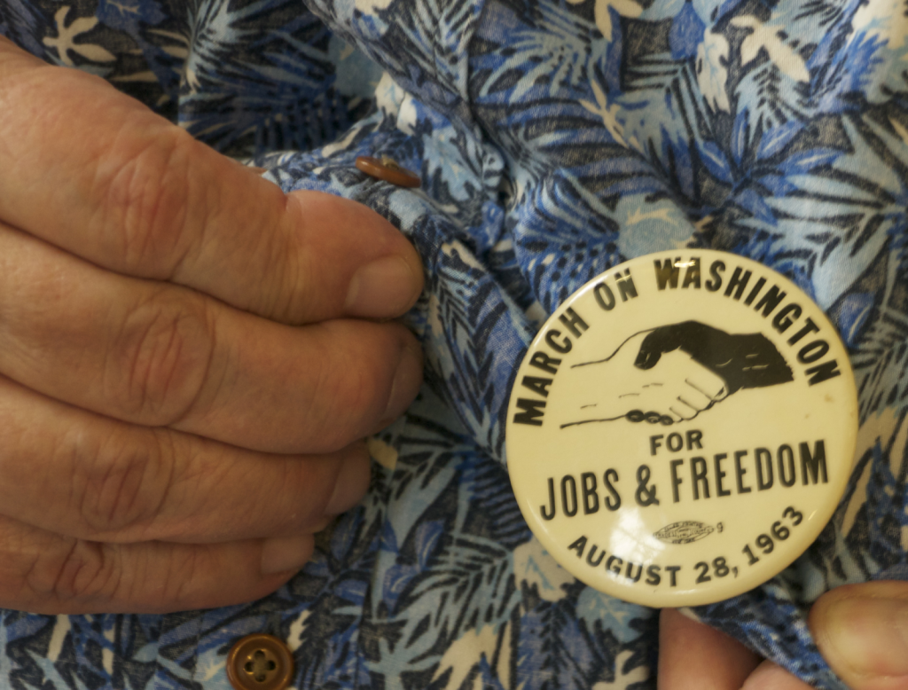Close-up of a pin Rev. Macdonell wears. It depicts a handshake between a Black person and a white person. Text reads: March on Washington for Jobs and Freedom. August 28, 1963.